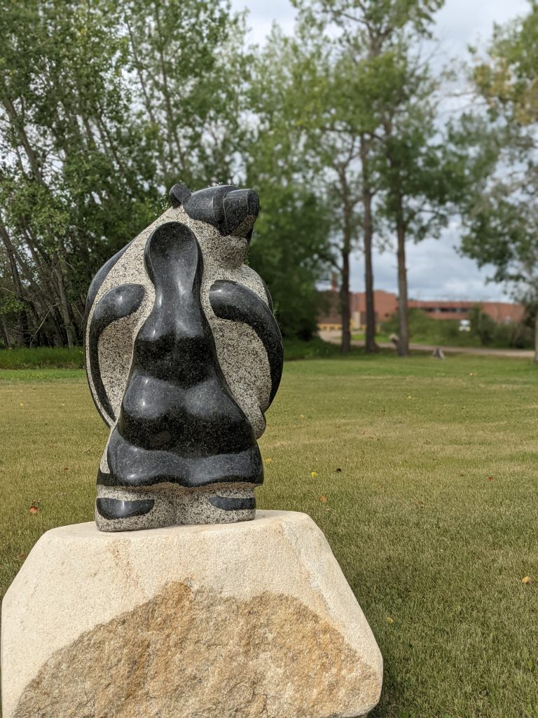 Image of one of the sculptures in the sculpture garden by Stewart Steinhauer, who hails from Saddle Lake Cree Nation. UnBQ school building in the background, August 2021. From Madisen Hvidberg.