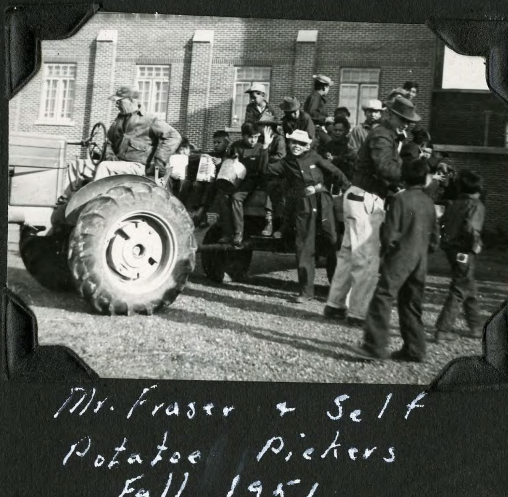 Grounds keeper Mr. Fraser and students heading to pick potatoes, fall 1951. Tractor is outside exit to the boys' playroom, with chapel in the background. Shingwauk Residential Schools Centre, Algoma University