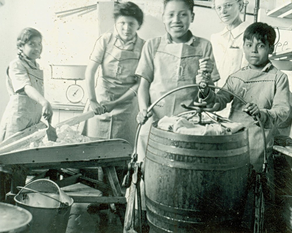 Four girls make butter in the kitchens down the hall from the boiler room. [194-?]. P75-103-S7-165 from the General Synod Archives, Anglican Church of Canada.