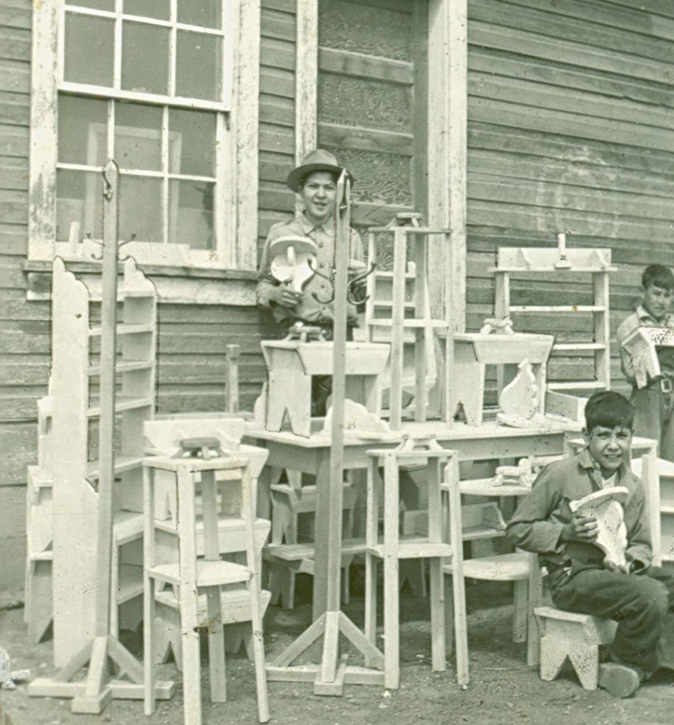 Display of finished items and three students from woodworking class. 1945. P75-103-S7-190 from the General Synod Archives, Anglican Church of Canada.