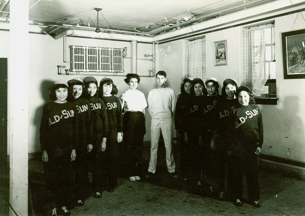 Old Sun School, Gleichen, Alberta - Girls' sports team and coaches, taken in student dining room - [194-?]. P7538-1012 from The General Synod Archives, Anglican Church of Canada