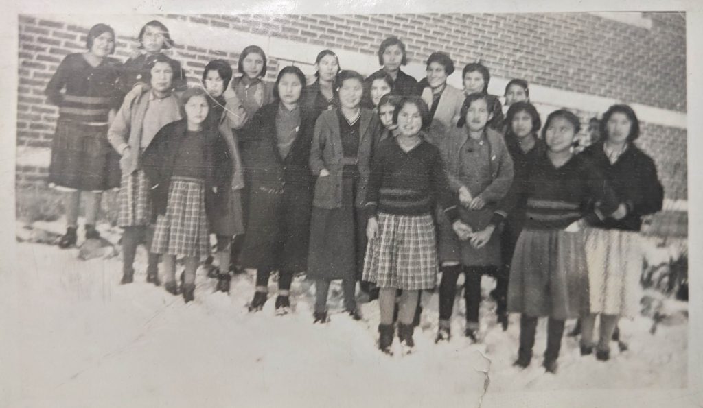 Choir girl outside of the main school building, 1936. PR1985.0100 from The Provincial Archives of Alberta, Open Copyright.