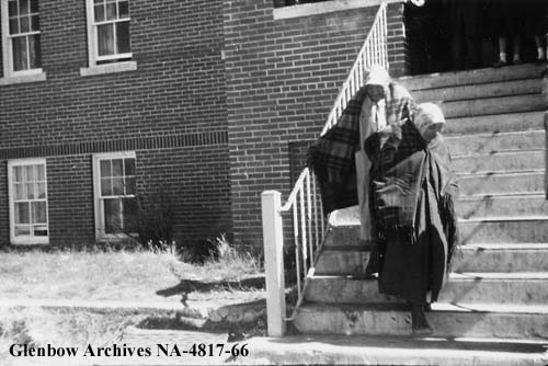 Mrs. Water Chief (right) and Mrs. Gunny Crow (left) on the steps of Old Sun after leaving church held in the school chapel. 1955-1957. NA-4817-66. Courtesy of Glenbow Archives .