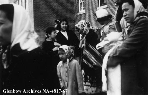 Women and children leaving Old Sun after church in the chapel. Despite community members attending services held in the Old Sun chapel, students were not allowed to speak with them. 1955-1957. NA-4817-67. Courtesy of Glenbow Archives .