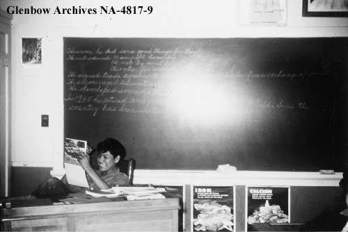 Duncan Winnipeg sits at a desk in a classroom. 1955-1957. NA-4817-9. Courtesy of Glenbow Archives .